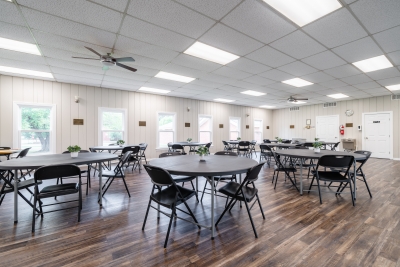 Photo of main room in community center, containing round tables and chairs