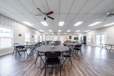 Photo of main room in community center, containing round tables and chairs