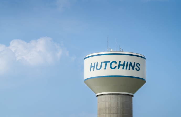 Photo of the watertower that says Hutchins on it, against the blue sky with a small white cloud